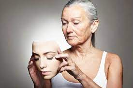 Immagine di una donna anziana che tiene in mano la maschera del suo viso da giovane